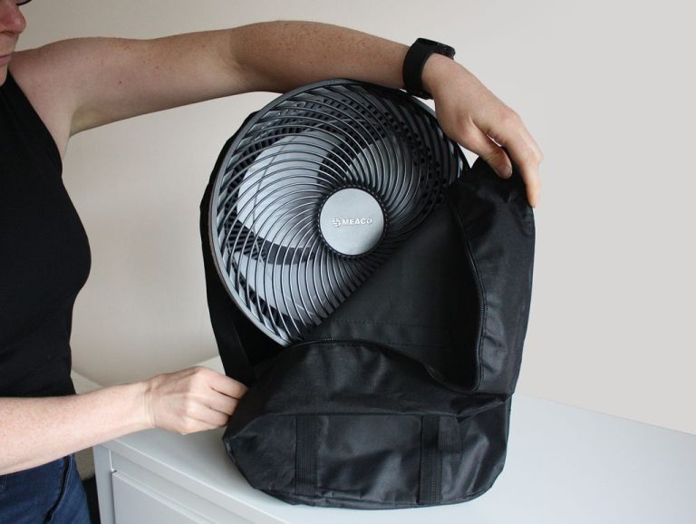 A person placing a Meaco SefteFan into a black zippered carrying case, holding the bag open with one hand while zipping it with the other.