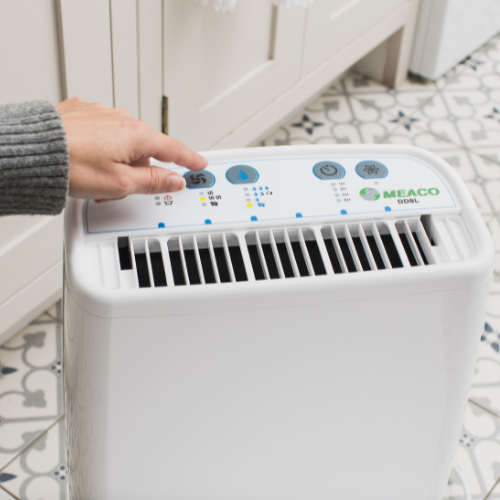 Lady's hand pressing a button on DD8L Dehumidifier set up in Utility room