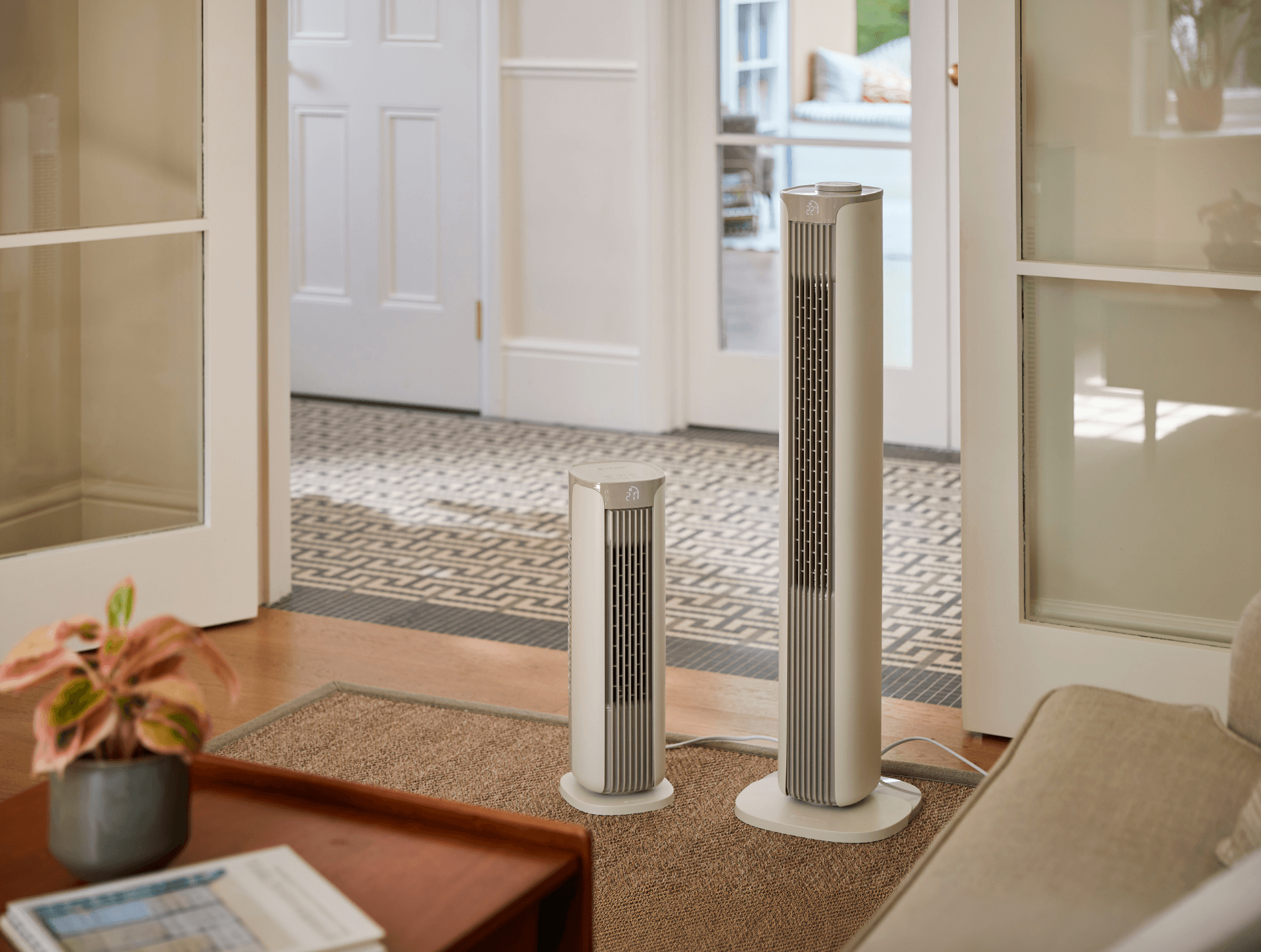 Meaco Sefte tower fans, both large and small, stand beside each other in a living room by open interior doors.